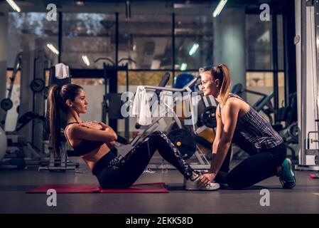 Side view of young motivated attractive healthy sporty active shape girl doing abs exercises and warming on the red mat while her young personal femal Stock Photo
