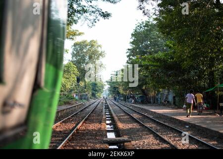 YANGON, MYANMAR - DECEMEBER 31 2019: The traditional circle train passing through a local platform stop with view over burmese people walking past Stock Photo
