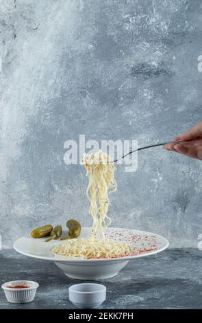 Female hand holding fork with noodles on marble background Stock Photo