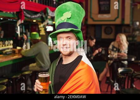 Portrait of happy young man in green hat drinking beer and celebrating Patricks Day in the pub Stock Photo