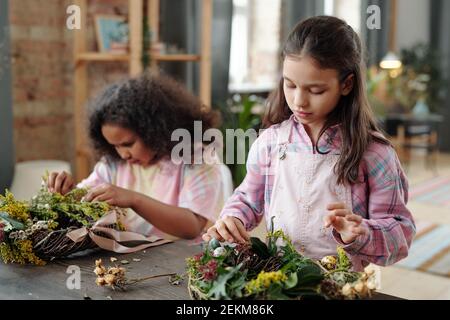 Cute children sitting at the table and decorating flower wreath for Easter at home Stock Photo