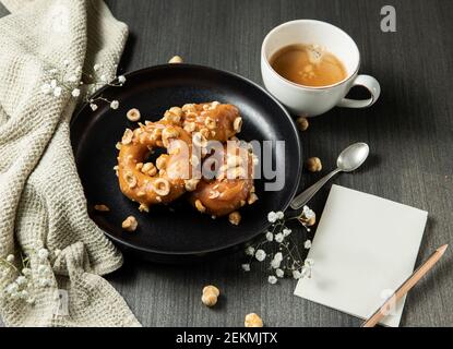 donuts with caramel and hazelnuts, cup of coffee on the rustic table Stock Photo