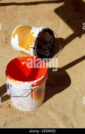 A couple of empty paint buckets stained with red and black paints left on the sandy ground Stock Photo