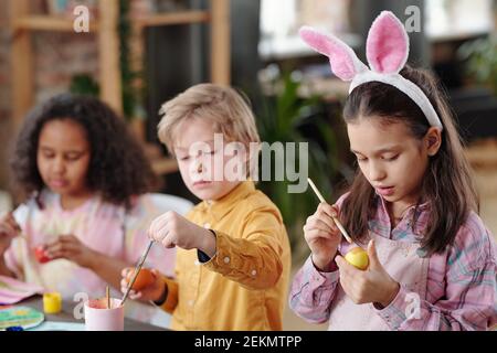 Children sitting at the table and painting Easter eggs together they preparing for the holiday Stock Photo