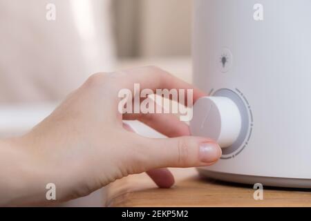 Woman turns on the modern air humidifier, aroma oil diffuser at home. Improving the comfort of living in a house, Improving the well-being. Ultrasonic Stock Photo