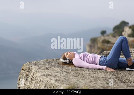 Happy woman wearing headphones listening to music in a cliff in the mountain Stock Photo