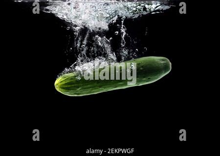 Whole bio cucumber sinking under water against black background Stock Photo