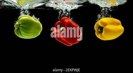 Three bell pepper or paprika green, red, yellow falling into the water and splash isolated on black background Stock Photo