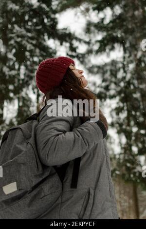 A girl in a red hat, looks at the sky, smiles, it is snowing, travel. Stock Photo