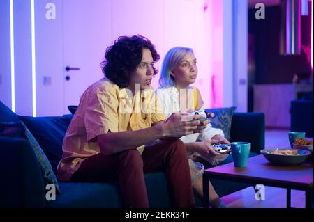 Handsome young man teaching how to play the video games to his girlfriend, on the couch, concept about home entertainment, video games. Stock Photo