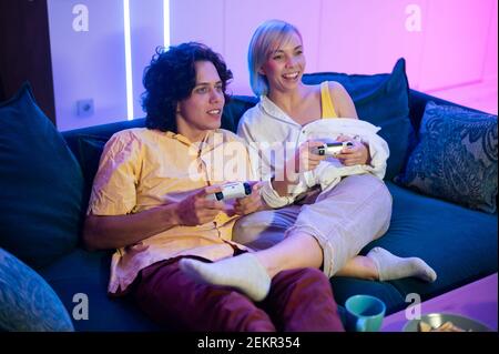 Handsome young man teaching how to play the video games to his girlfriend, on the couch, concept about home entertainment, video games. Stock Photo