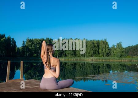 Young female practicing yoga against the sky on a sunrise. Pretty slim woman performs an exercise. Healthcare, meditaion, welness, mindfulness concept Stock Photo