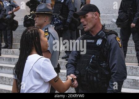 Mia Wells, 19, of Columbus, Ohio shakes Ohio State Trooper’s hand on the steps of the Ohio Statehouse. Wells was deeply moved by the State Troopers’ gesture to take a knee in honor of those killed by racism and police brutality.Large groups of protestors gathered in front of the Ohio Statehouse to protest against police brutality, and the killing of George Floyd by Minneapolis Police Officer Derek Chauvin on May 25, 2020. People protested from 5pm to 10:30pm when the protesters were dispersed by the Riot Police for breaking the 10pm curfew. The day of protest involved marked moments of marchin Stock Photo