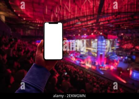 Man's hand using digital application on the mobile smart phone at esport event at big arena. Blank screen with copy space. Stock Photo