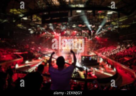 Abstract blurred background of big esports gaming event at big arena. Man with a hands raised. Stock Photo