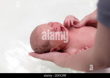 Crying baby by in a bathtub. Infant kid sreaming while taking a bath