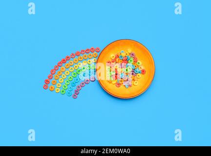 Bowl of multicolored cereals and a cereal rainbow, isolated on a blue-colored background. Breakfast table, flat lay. Fruit rings multigrain cereals. Stock Photo