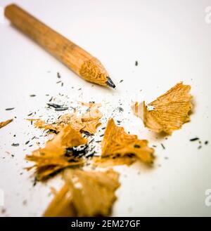 A close-up view of a sharpened pencil surrounded by wooden shavings on a white surface Stock Photo