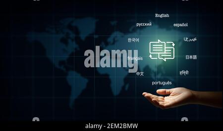 Hand holding speech bubble with arrows and text in many important languages. Illustration of World map background. Translator and languages education Stock Photo