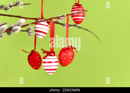 Red and white Easter eggs with stripes and dots hanging from goat willow branch on green background Stock Photo