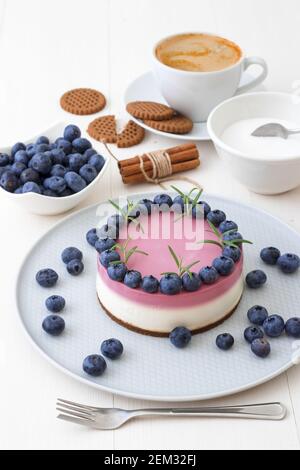 The two-color blueberry mini cheese cake. Round no bake cheesecake, cut portion on small plate with few cookies in the focus. The top of cake decorate Stock Photo