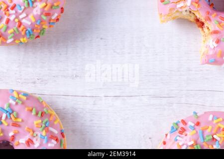 Delicious donuts with pink icing, strawberry jelly filling and colorful sprinkles on wooden background with copy space. Sweet American pastry. Stock Photo