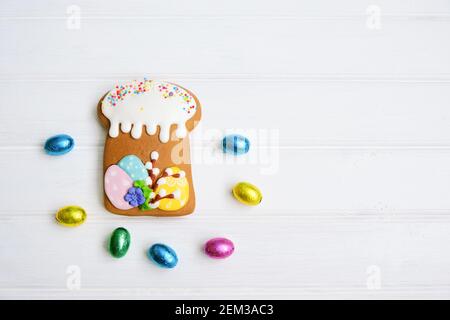 Gingerbread in the form of a cake and colorful chocolate eggs on a white wooden background. Sweets for celebrating Easter. Stock Photo