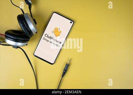 Clubhouse app logo displayed on a smartphone screen with headphones on yellow background. Popular trending audio chat Stock Photo