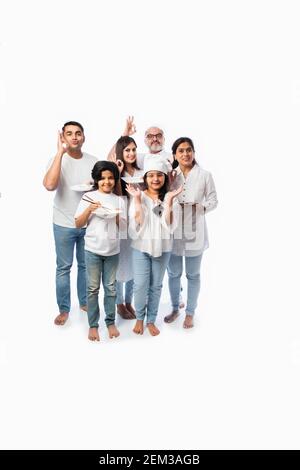 Multigenerational Indian family of six holding empty plate and bowls while little girl chef wears hat Stock Photo