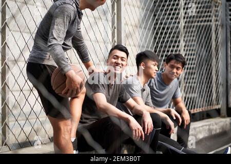 group of four asian young adult men resting relaxing talking chatting on outdoor basketball court Stock Photo