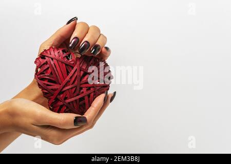 Wicker red heart made of straw in woman's hands on white background. Happy Valentines day or love concept. Stock Photo