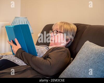 Senior woman resting on a settee engrossed in her tablet computer, UK Stock Photo