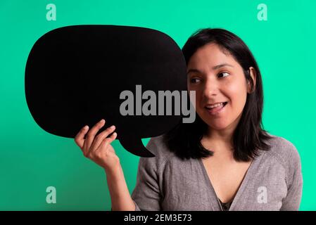 young hispanic woman smiling and looking at black empty bubble with surprise, concept of ideas and imagination. empty cloud with copy space. green stu Stock Photo
