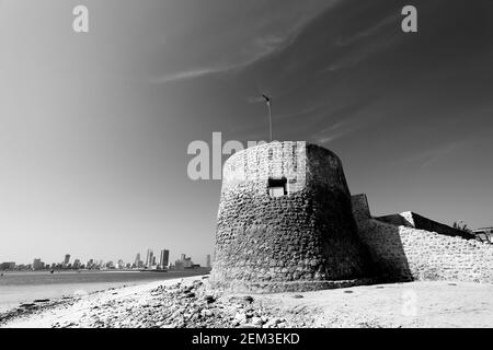 Monochrome, black and white, image of Bu Maher Fort, the start of Bahrain’s Pearl Trail, Manama in the background, Muharraq, Kingdom of Bahrain Stock Photo