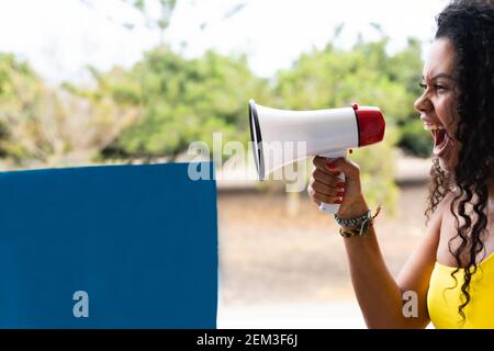 Funny young brunette woman girl screaming in megaphone. People sincere emotions lifestyle concept. Blue banner for copy space. Stock Photo