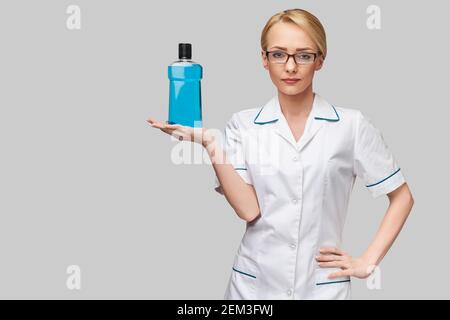 woman dentist doctor holding bottle of mouthwash standing over grey background Stock Photo