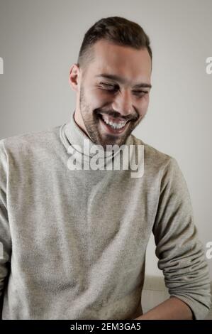 Portrait of a young man with a short beard that laughs cheerfully during a conversation Stock Photo