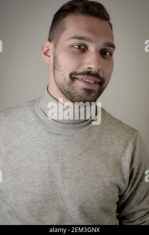 Portrait of a smiling young brown-haired man with a short beard and a gray turtleneck sweater Stock Photo