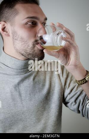 Portrait of a young man with a short beard who drinks a glass of beer Stock Photo