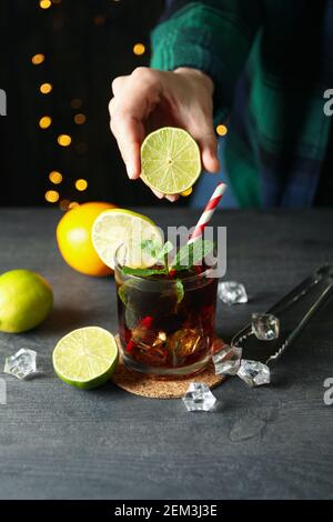 Woman squeeze lime in Cuba Libre cocktail against blurred lights Stock Photo