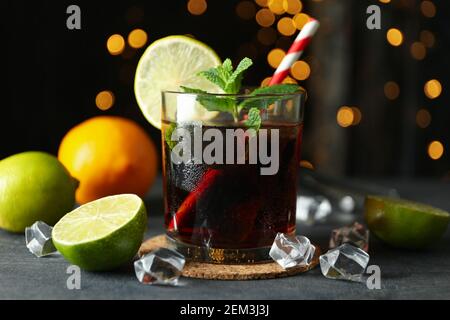 Glass of Cuba Libre on gray textured table against blurred lights Stock Photo