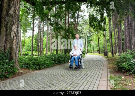 Senior man pushing his wife in wheelchair through the park Stock Photo