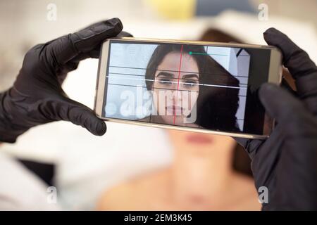 Checking of facial symmetry and balance with mobile phone app Stock Photo