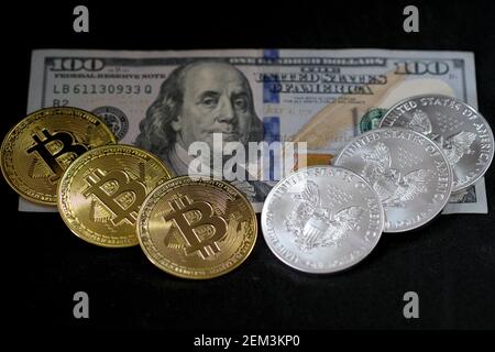 In this photo illustration, visual representations of the digital cryptocurrency, Bitcoin, and 1oz silver American Eagle bullion coins are placed on a US 100 dollar bill on February 20, 2021 in Katwijk, Netherlands.  (Photo by Yuriko Nakao/AFLO) Stock Photo