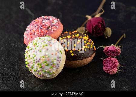 Sweet small doughnuts with sprinkles on a black background Stock Photo
