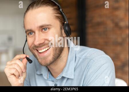Handsome European man with headset looking away and talking, has a light brown hair, gray eyes and beard, smiling friendly, operator call-center Stock Photo