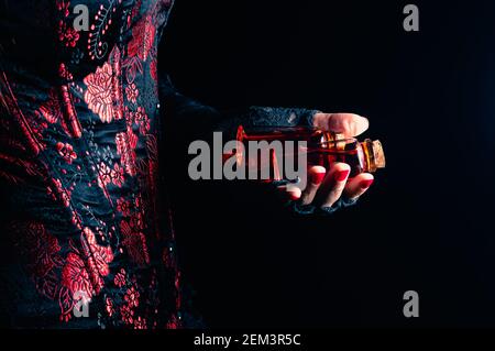 Someone wearing a black and red corset and black lace gloves holding two glass stopper bottles with red liquid Stock Photo