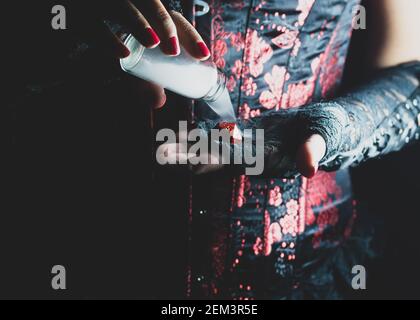 Someone wearing a black and red corset and black lace gloves pouring smoke from a glass bottle on to a red rpg die Stock Photo