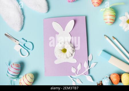 Diy Easter card from paper. greeting cards with bunny on blue background. Gift idea, decor Spring, Easter. Top view. Process kid children craft. Stock Photo