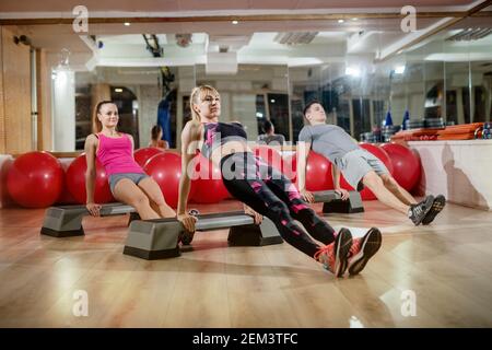 Attractive healthy shape active sporty fitness group doing Purvottanasana upward plank pose on the steppers in the gym. Stock Photo